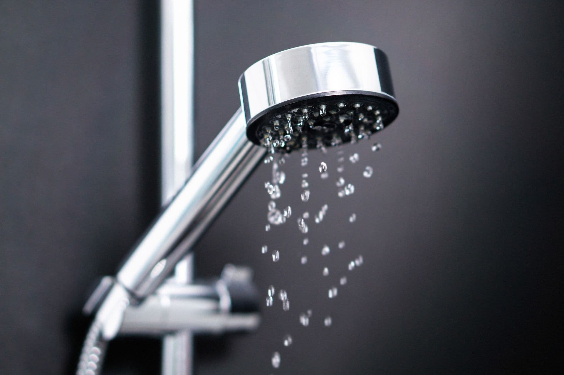 Close-up of a chrome showerhead with water droplets streaming down against a dark background, conveying a fresh and modern bathroom feel.