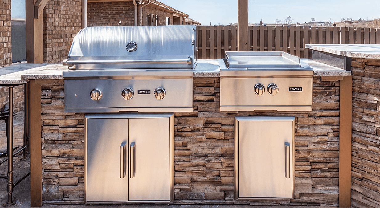 Modern outdoor kitchen with stainless steel grill and side burner set into a stone island. The setting is sunny, exuding a clean, inviting vibe.