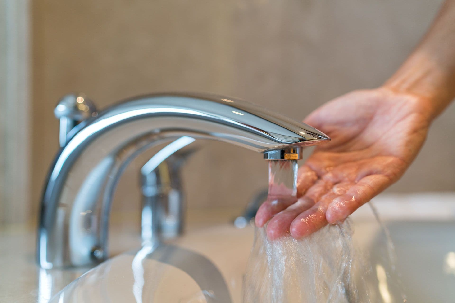 A close-up of a shiny, silver faucet with water flowing into an outstretched hand.