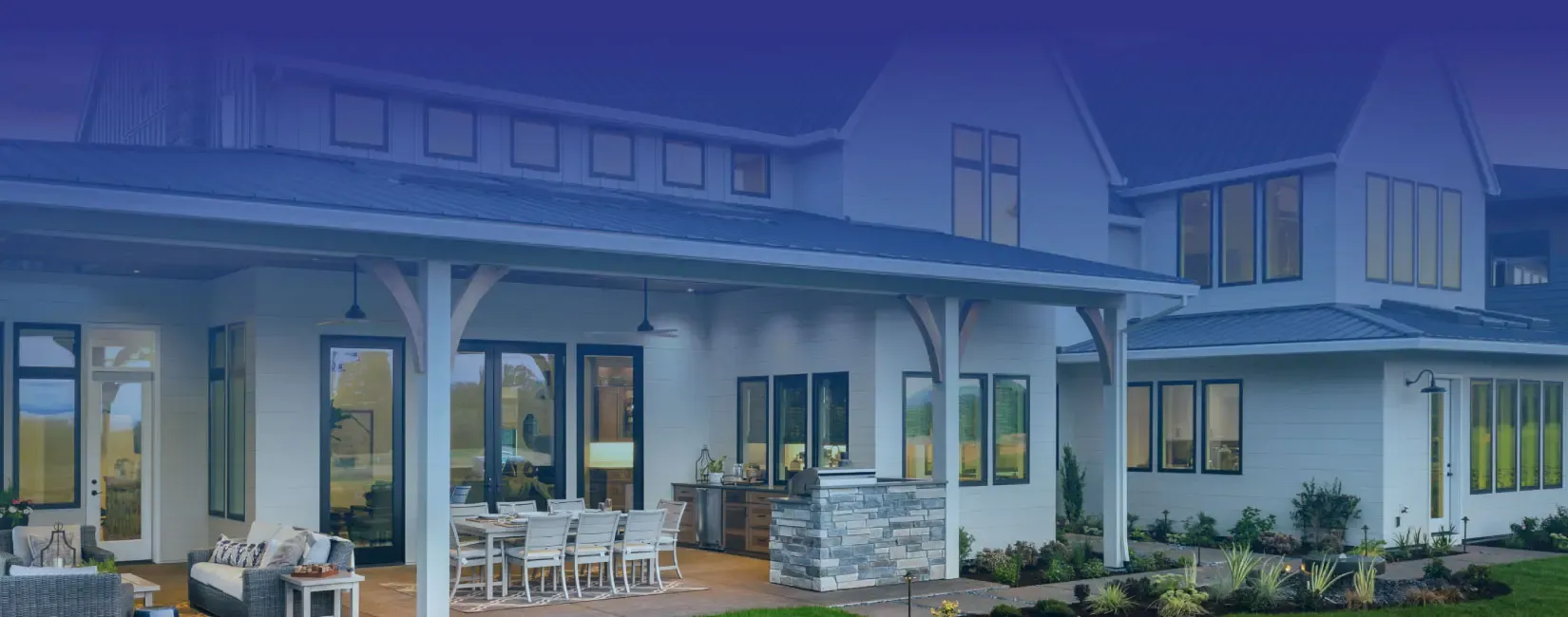 Spacious modern house with large windows and covered patio. Outdoor seating and dining area create a welcoming, luxurious atmosphere.