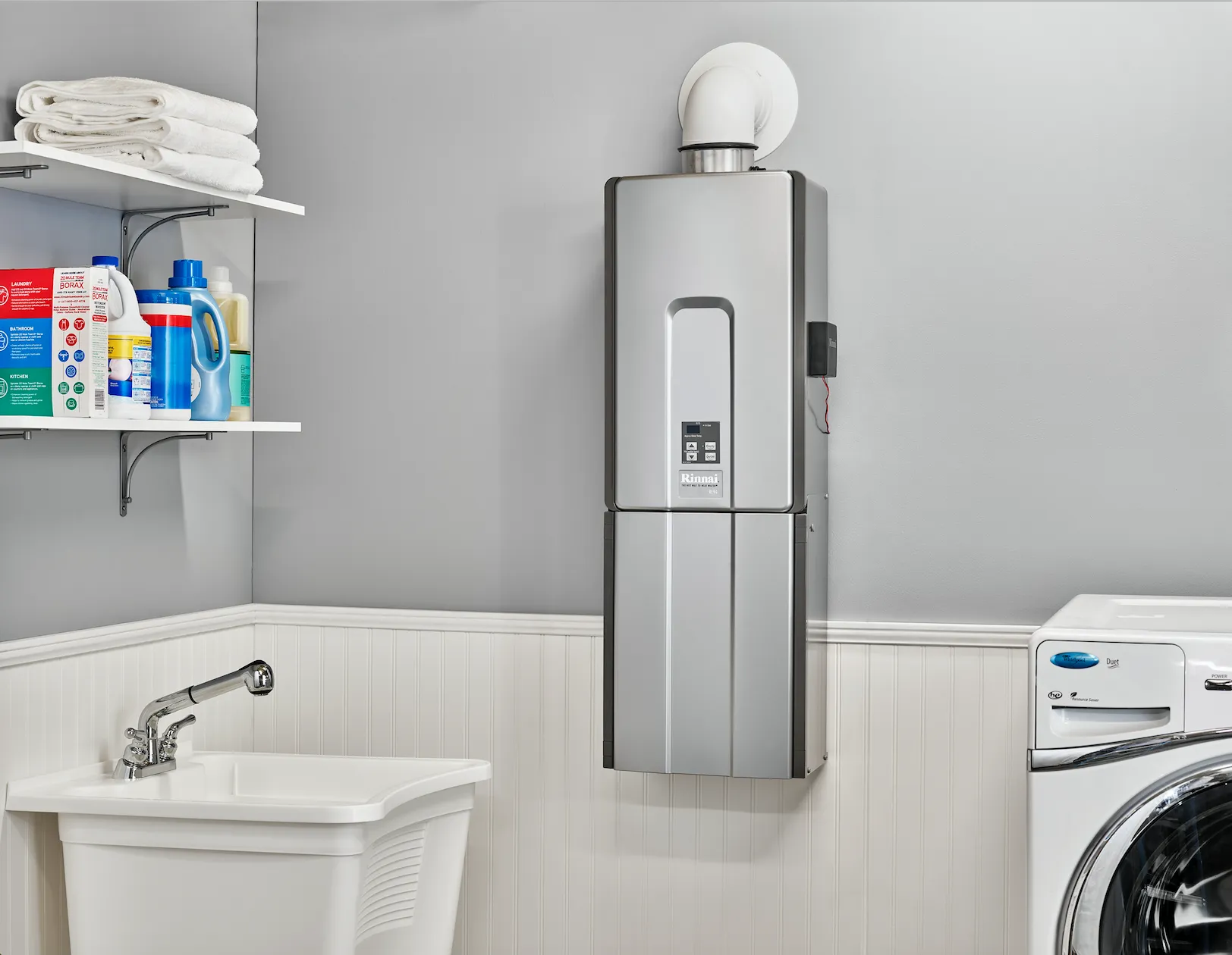 Modern laundry room with a sleek, wall-mounted water heater. Nearby are shelves with detergent and towels, a sink, and a washing machine.